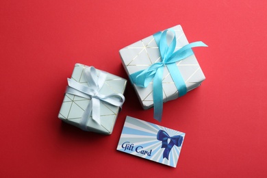 Photo of Gift card and presents on red background, flat lay