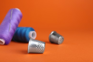 Photo of Thimbles, spools of sewing threads and needle on orange background, space for text