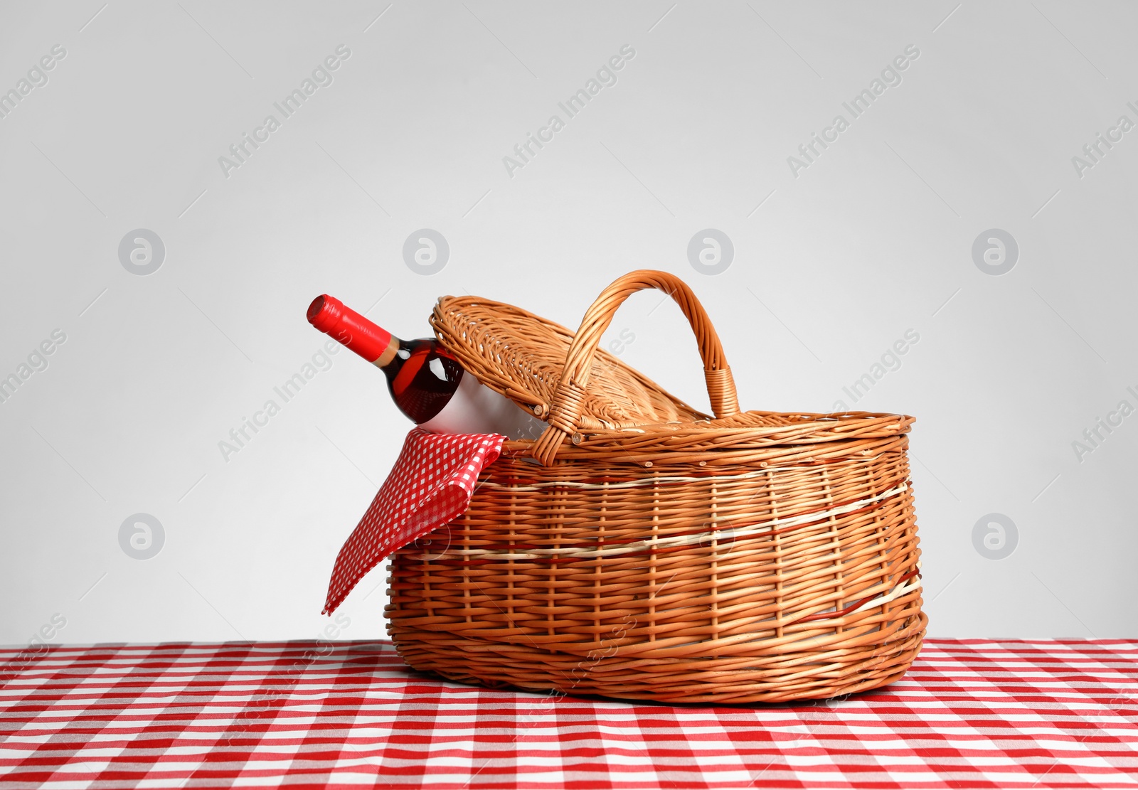 Photo of Picnic basket with bottle of wine on checkered tablecloth against white background