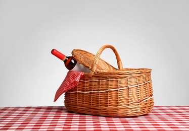 Photo of Picnic basket with bottle of wine on checkered tablecloth against white background