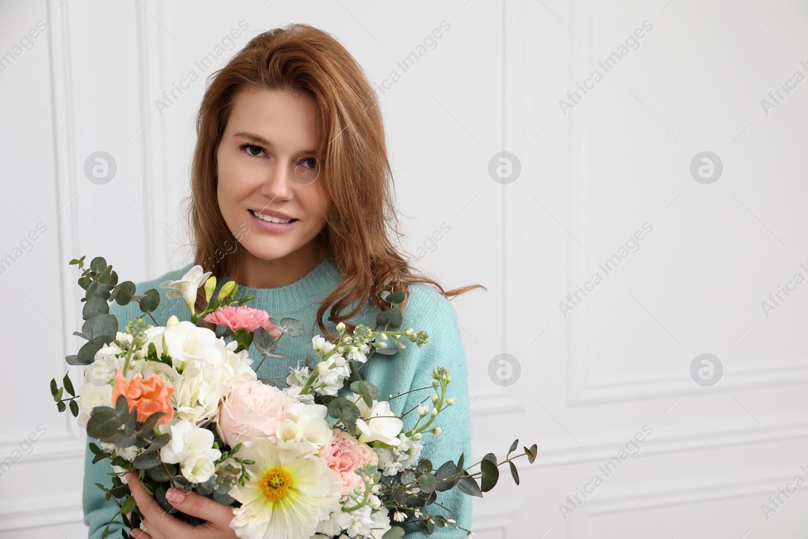 Photo of Beautiful woman with bouquet of flowers near white wall indoors. Space for text