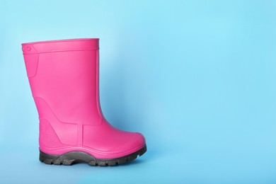 Photo of Bright pink rubber boot on light blue background. Space for text