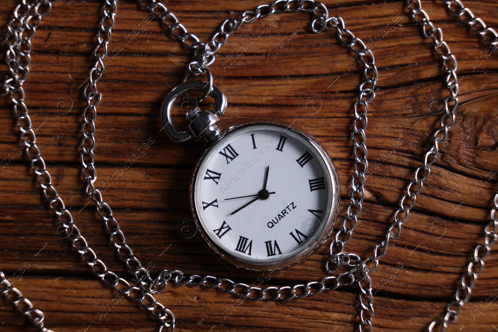 Photo of Silver pocket clock with chain on wooden table, top view