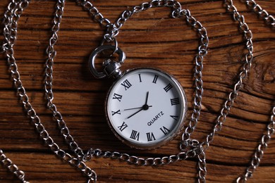 Silver pocket clock with chain on wooden table, top view