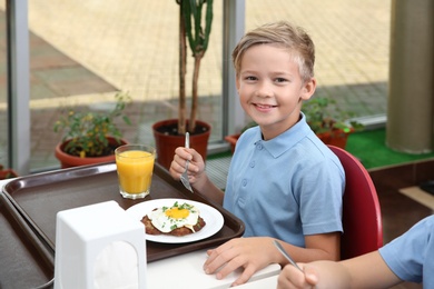 Photo of Cute boy at table with healthy food in school canteen