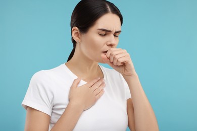 Woman coughing on light blue background. Cold symptoms