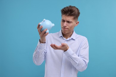 Upset man with piggy bank on light blue background