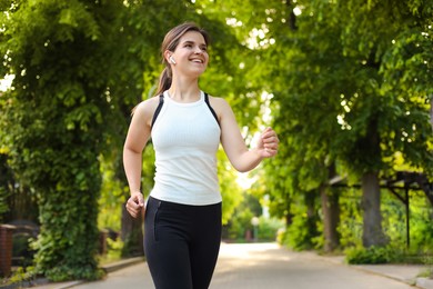 Young woman with wireless earphones jogging outdoors in morning