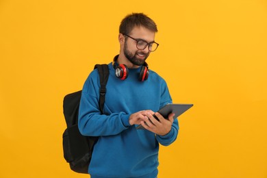 Photo of Student with headphones and backpack using tablet on yellow background