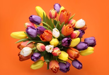 Photo of Bouquet of beautiful colorful tulips on orange background, top view