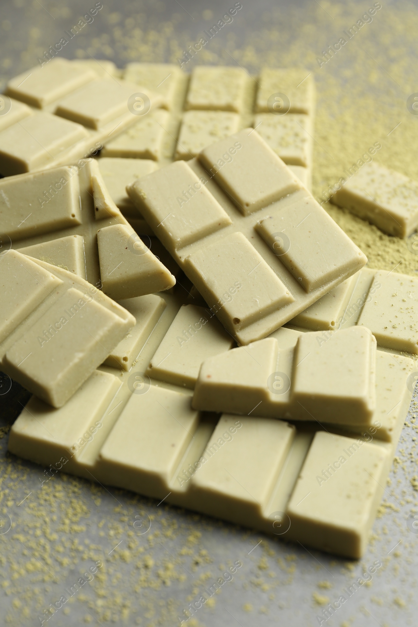 Photo of Pieces of tasty matcha chocolate bars and powder on grey table, closeup