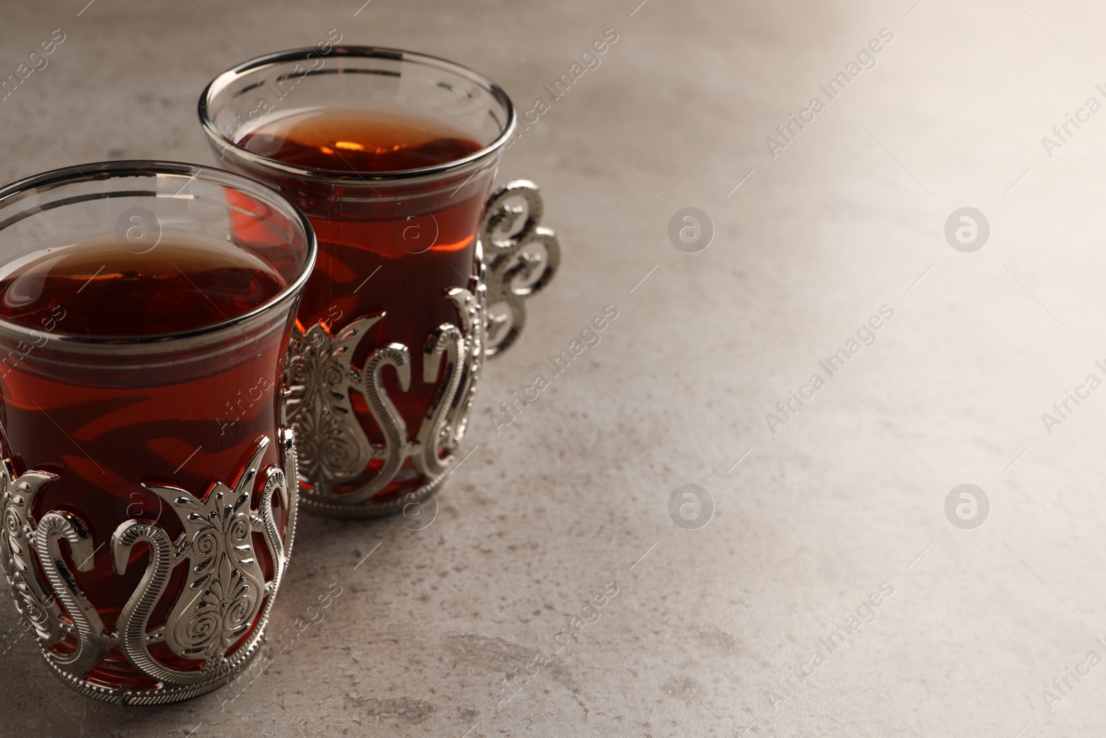 Photo of Glasses of traditional Turkish tea in vintage holders on light grey table, closeup. Space for text