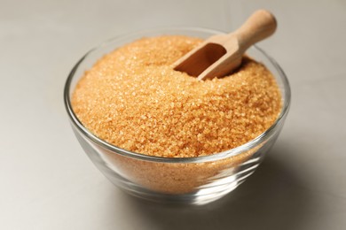Photo of Brown sugar and scoop in glass bowl on light grey table, closeup
