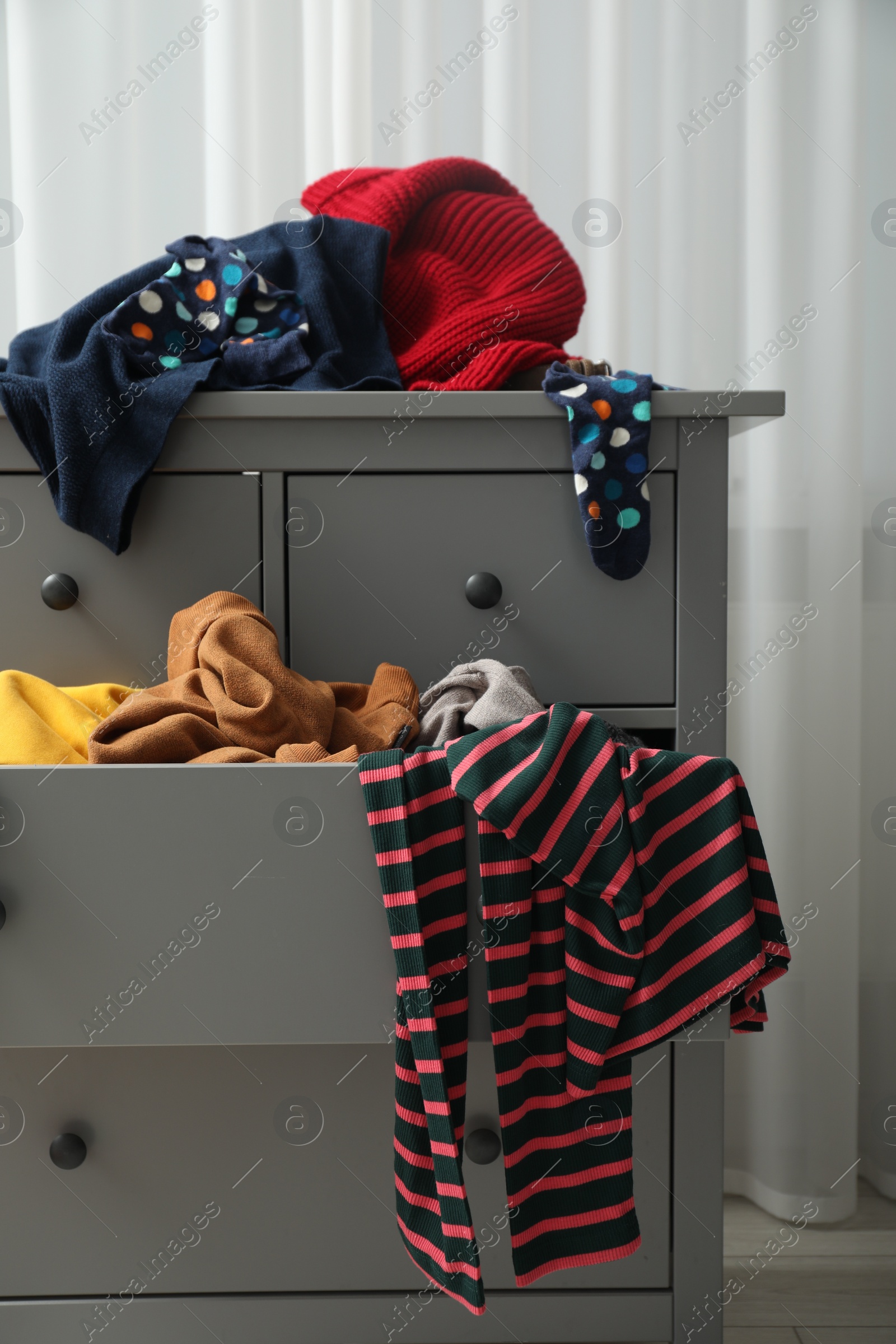 Photo of Cluttered chest of drawers indoors. Clothes in mess