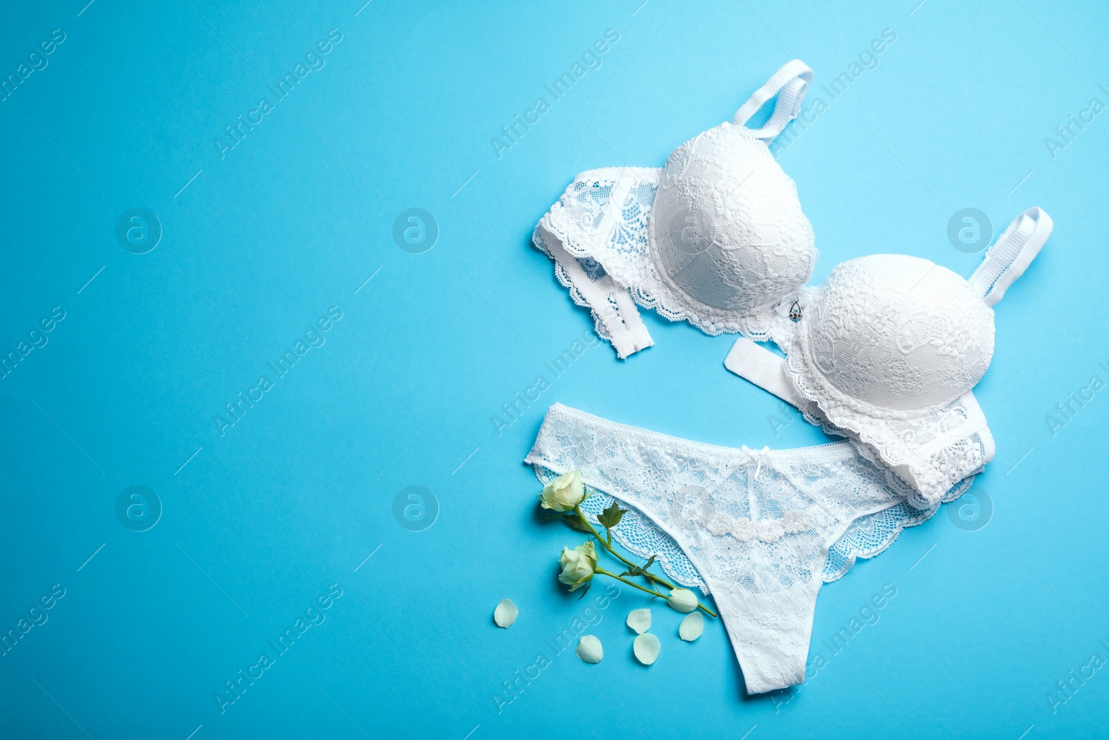 Photo of Elegant women's underwear and flowers on light blue background, flat lay. Space for text
