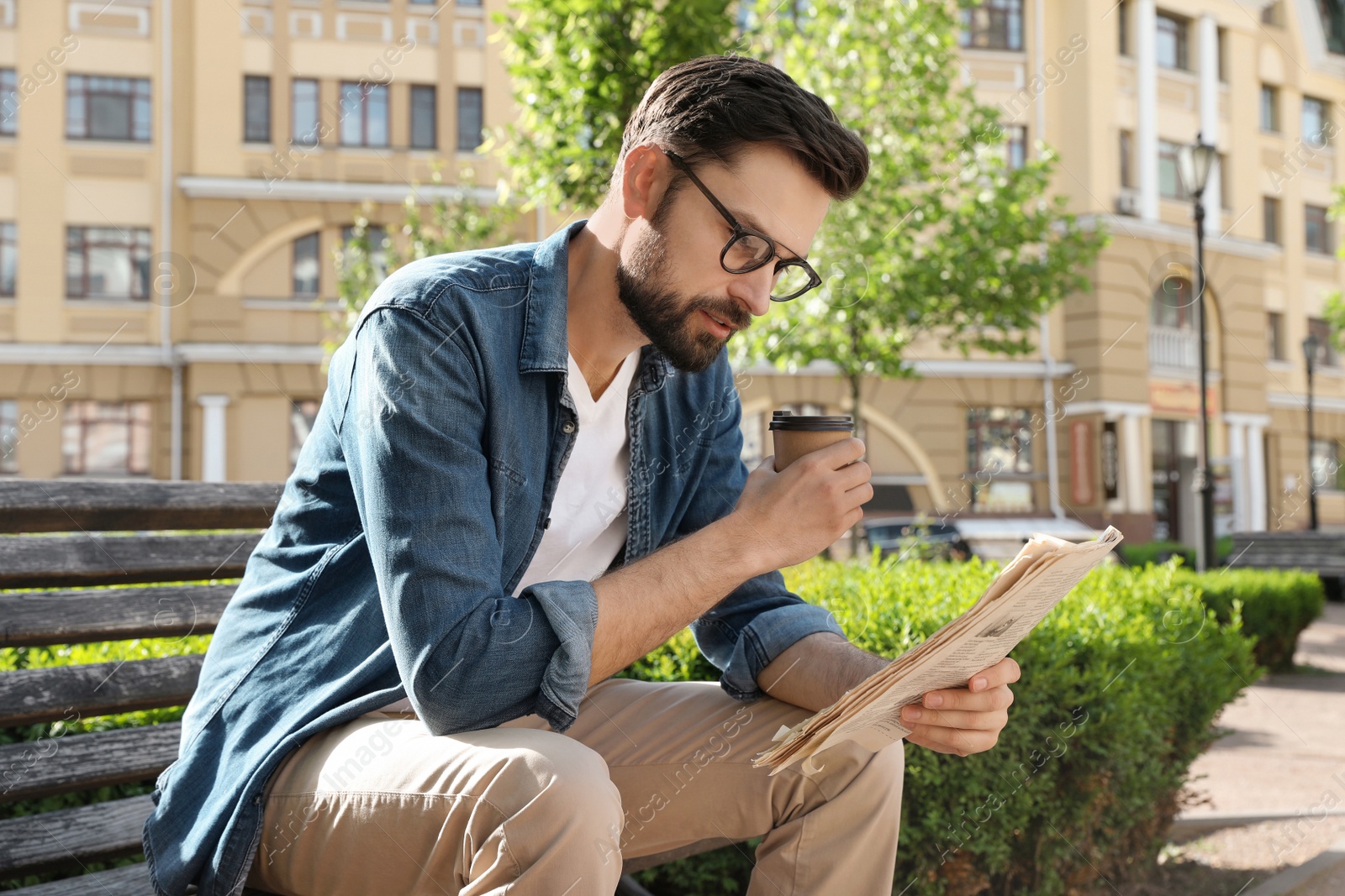 Photo of Handsome man reading newspaper on bench in park