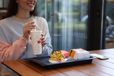 Photo of Lviv, Ukraine - September 26, 2023: Woman with McDonald's drink, burger and french fries at wooden table in restaurant, closeup