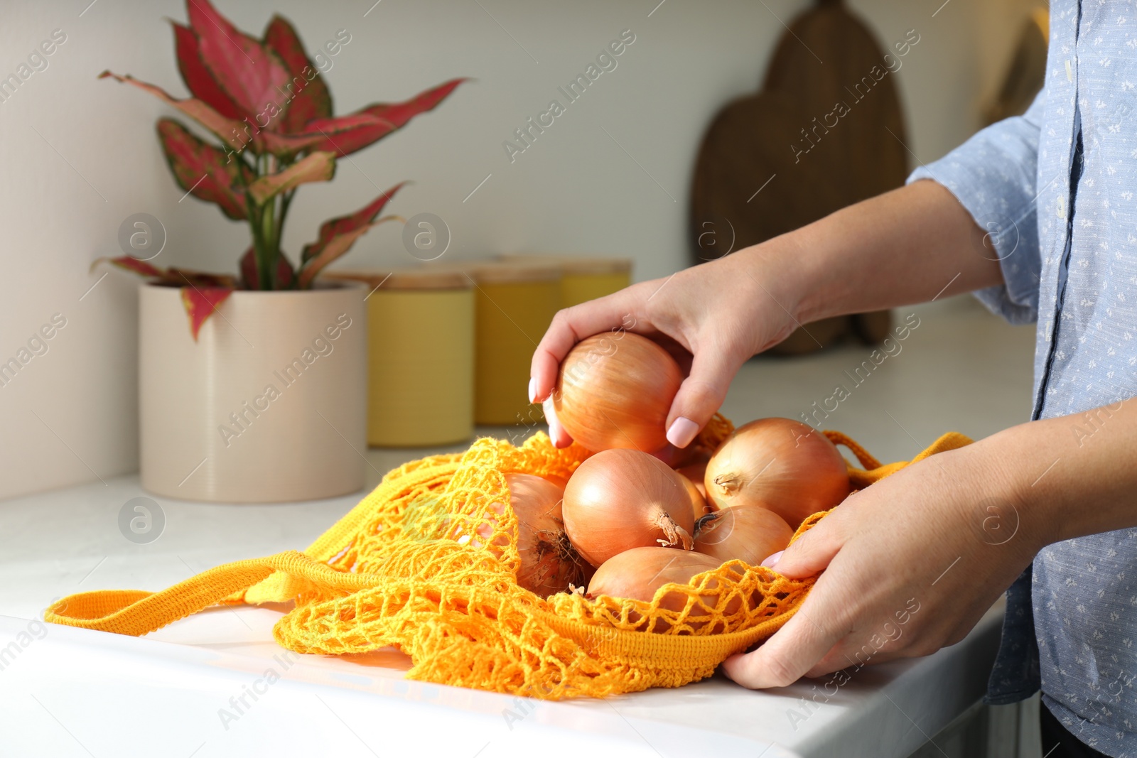 Photo of Woman taking golden onion from mesh tote bag at countertop in kitchen, closeup