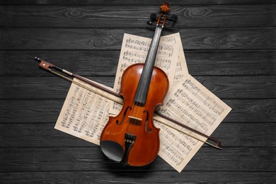 Photo of Violin, bow and music sheets on black wooden table, top view