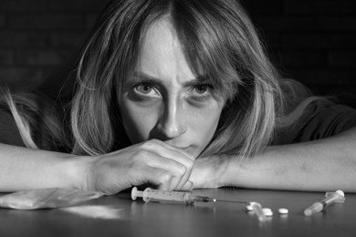 Photo of Addicted woman at table with different drugs, black and white effect