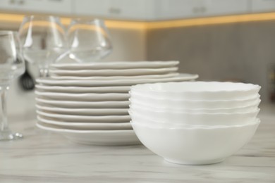 Photo of Clean plates, bowls and glasses on white marble table in kitchen