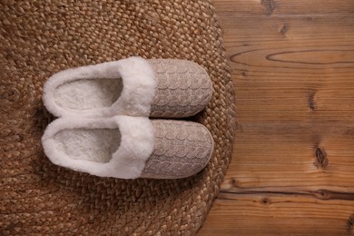 Pair of warm stylish slippers and wicker mat on wooden floor, flat lay. Space for text