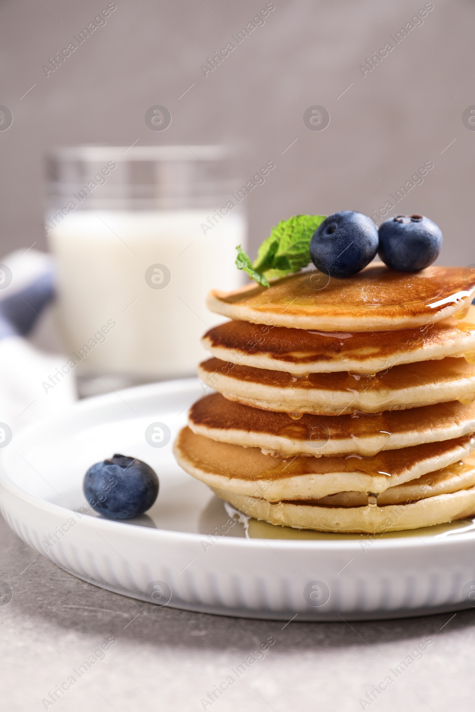 Photo of Plate of tasty pancakes with blueberries and honey on light grey table