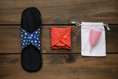 Reusable cloth pads and menstrual cup on wooden table, flat lay