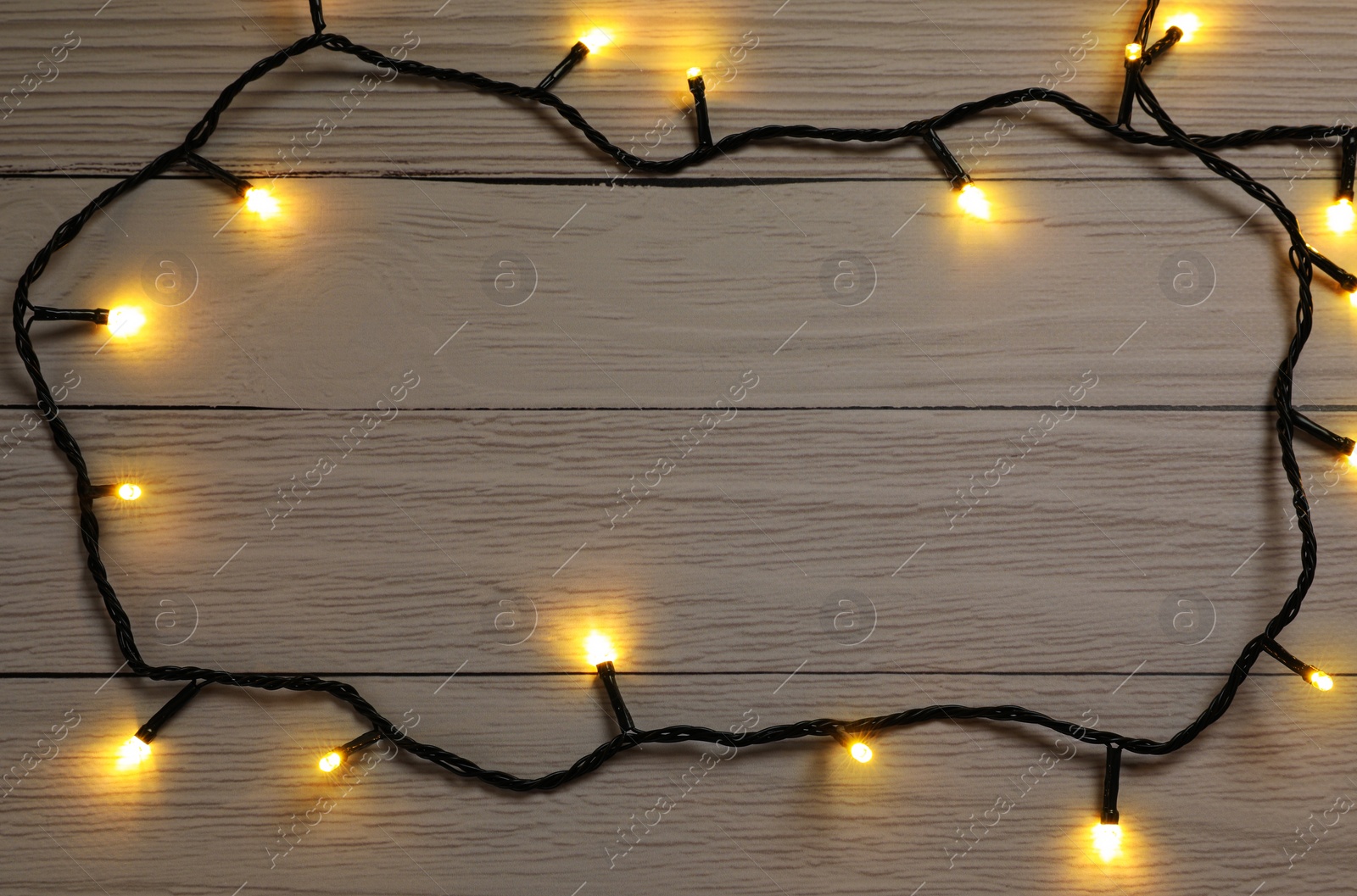 Photo of Glowing festive lights on wooden background, top view. Space for text