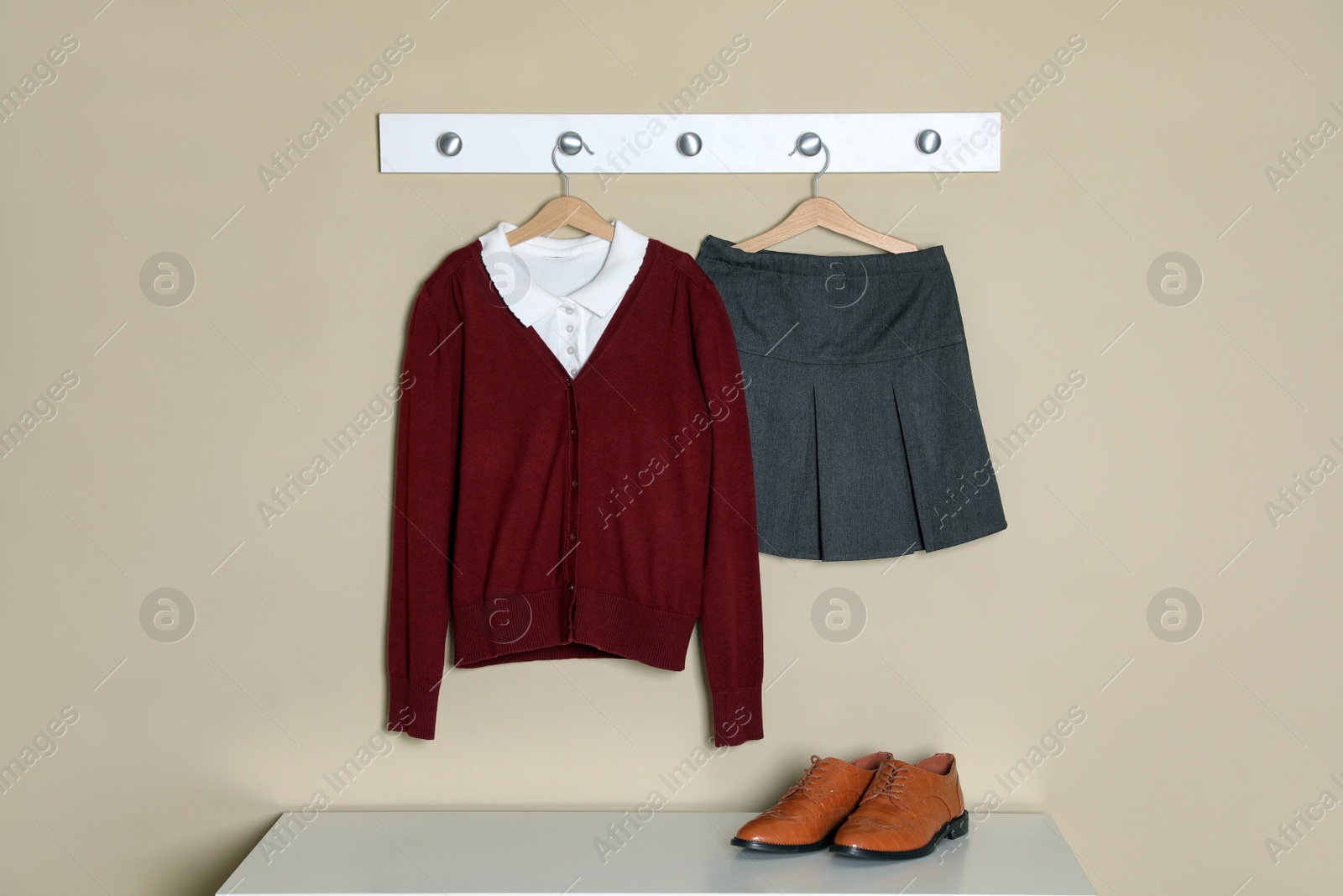 Photo of Shirt, jumper and skirt hanging on beige wall. School uniform