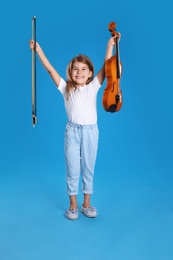 Photo of Little girl with violin and bow on light blue background