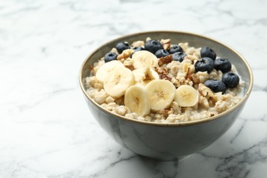 Photo of Tasty oatmeal with banana, blueberries, walnuts and milk served in bowl on white marble table, space for text
