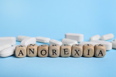 Photo of Word Anorexia made of wooden cubes with letters near pills on light blue background