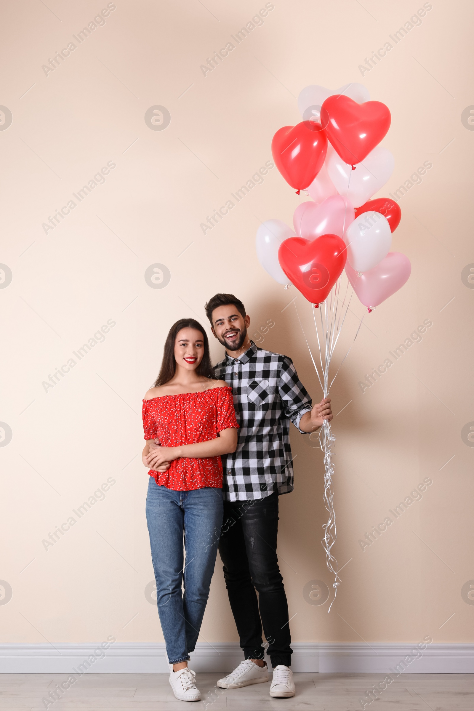 Photo of Happy young couple with heart shaped balloons near beige wall. Valentine's day celebration