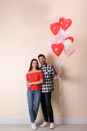 Photo of Happy young couple with heart shaped balloons near beige wall. Valentine's day celebration