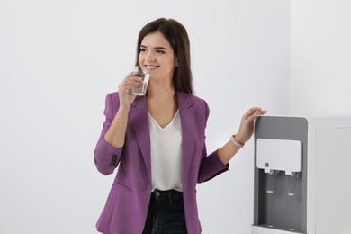 Photo of Young woman having break with glass of water near cooler in office