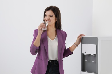 Young woman having break with glass of water near cooler in office