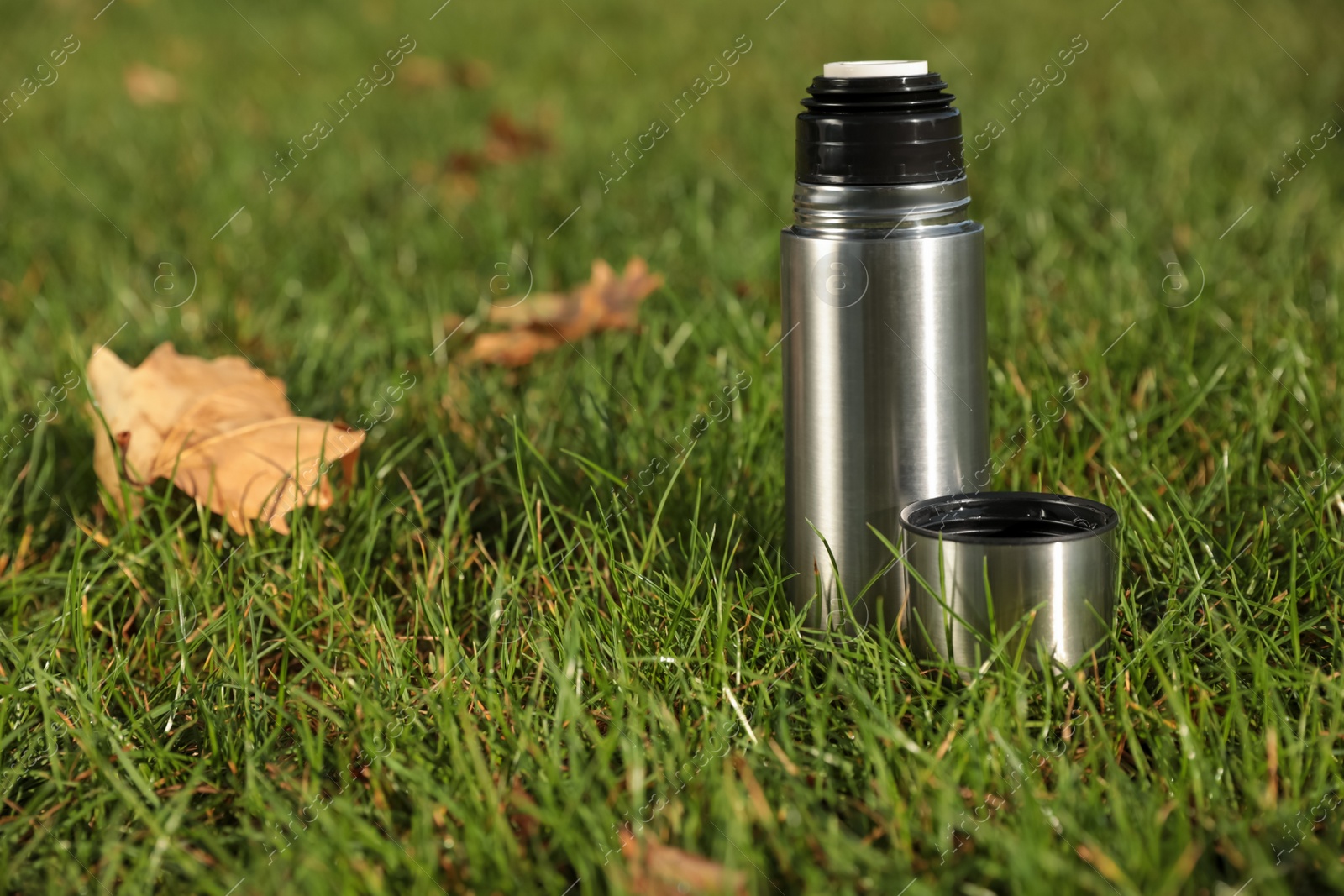 Photo of Modern silver thermos on green grass outdoors. Space for text