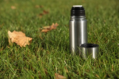 Photo of Modern silver thermos on green grass outdoors. Space for text