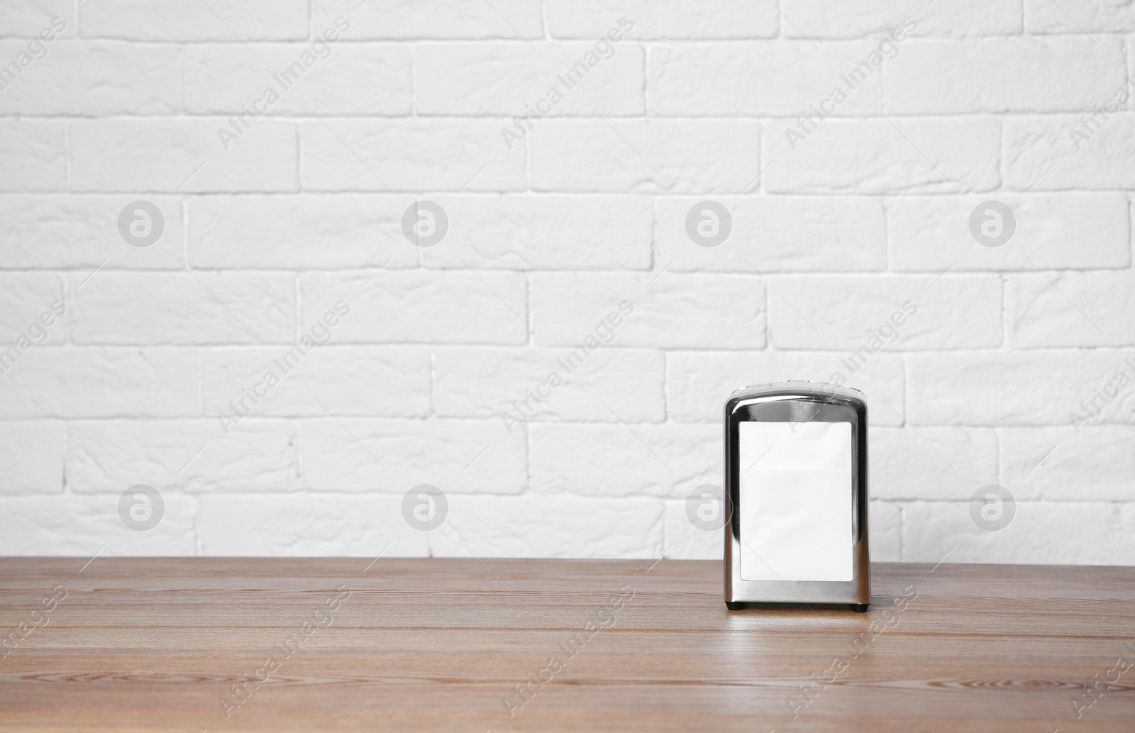 Photo of Napkin holder with paper serviettes on table against brick wall. Space for text