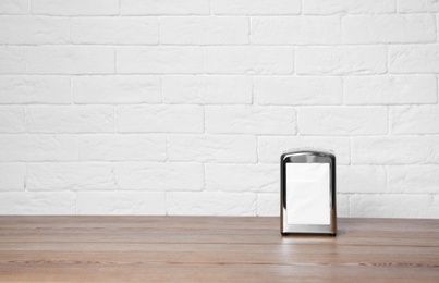 Photo of Napkin holder with paper serviettes on table against brick wall. Space for text