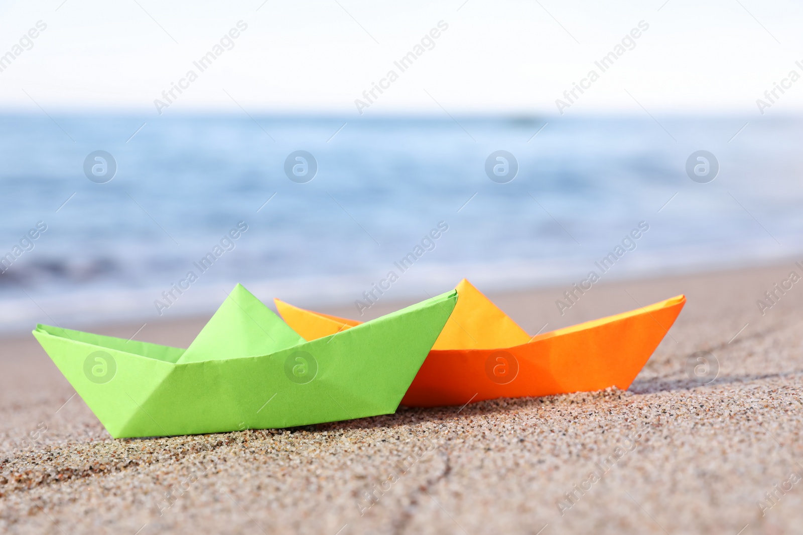 Photo of Bright color paper boats on sandy beach near sea