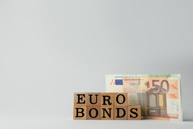 Photo of Word Eurobonds made of wooden cubes with letters and banknotes on light grey background. Space for text
