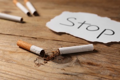 Broken cigarette and word Stop written on paper on wooden table, closeup. No smoking concept