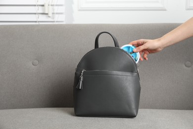 Photo of Woman putting pill box into backpack on sofa, closeup