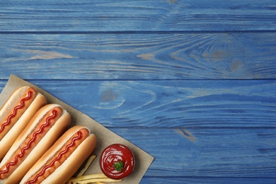 Composition with hot dogs, french fries and sauce on color wooden table, top view. Space for text