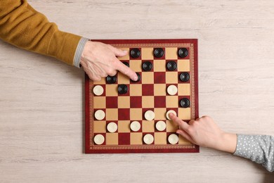 Photo of Senior man playing checkers with woman at white wooden table, top view