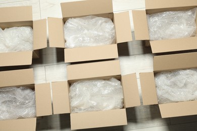 Many open cardboard boxes with bubble wrap on white wooden floor, flat lay
