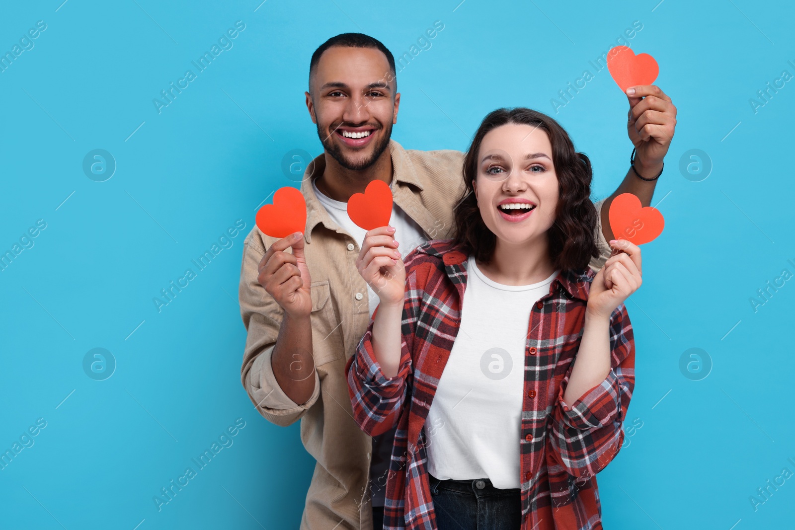 Photo of Lovely couple with red paper hearts on light blue background, space for text. Valentine's day celebration