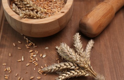 Photo of Mortar, pestle and ears of wheat on wooden table, closeup